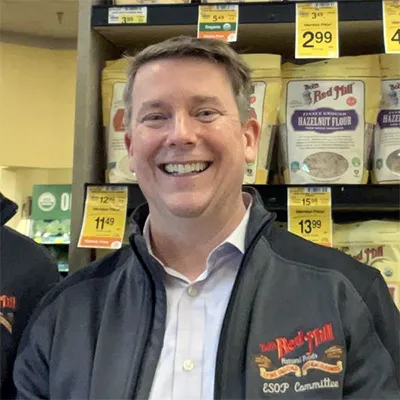 A photo of a man in front of Bob's red mill products on a shelf
