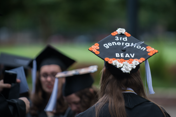 A person at graduation wearing a hat that says third generation beaver