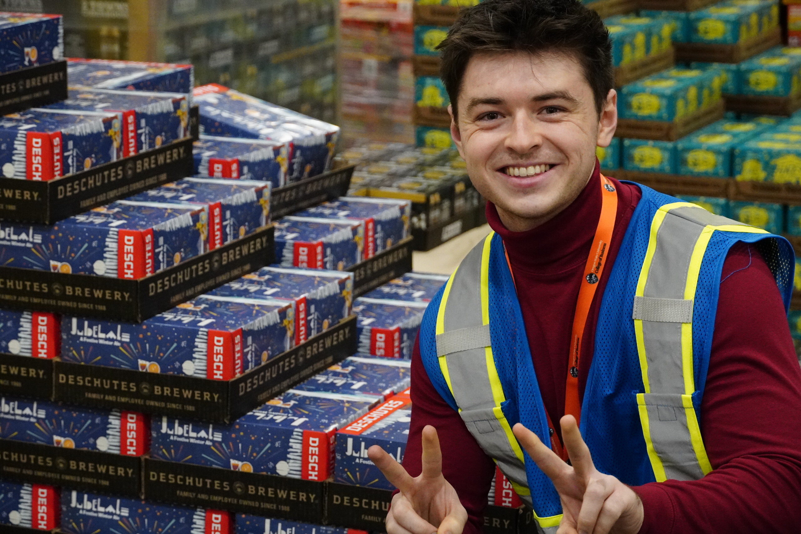 A headshot of a man wearing a hi-vis vest posing in front of a palette of Deschutes Brewery product.