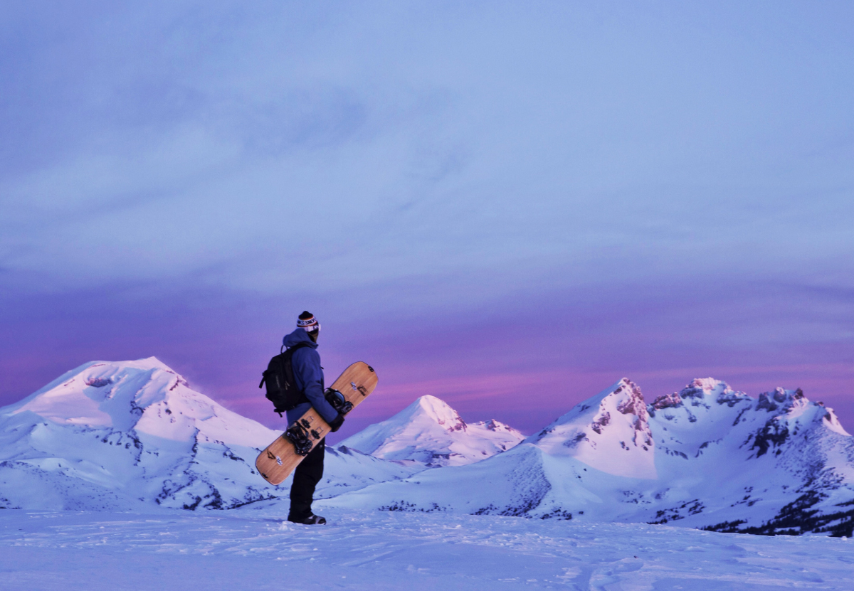 three OSU College of Business snoplanks academy snowboarders in the distance holding their boards up over their heads