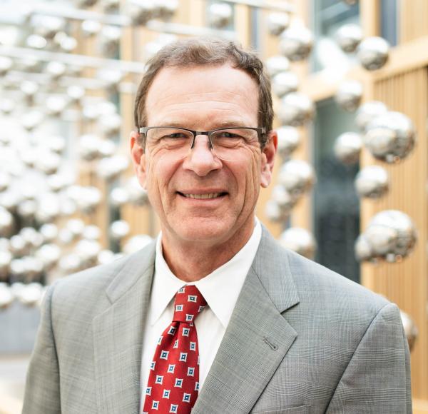 Jay Price, wearing a suit and tie, stands smiling while looking toward the camera.