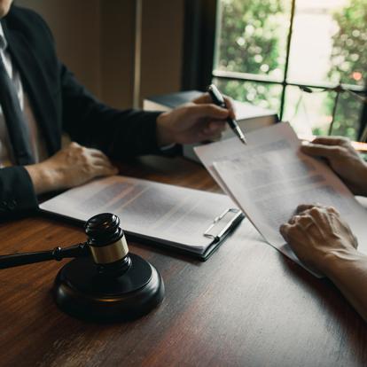 two people signing a contract next to a gavel