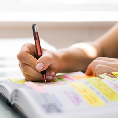 person writing in a book with lots of colorful tabs inside of it