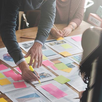 a group of people overlooking printed pages with lots of sticky notes on them as one person highlights something