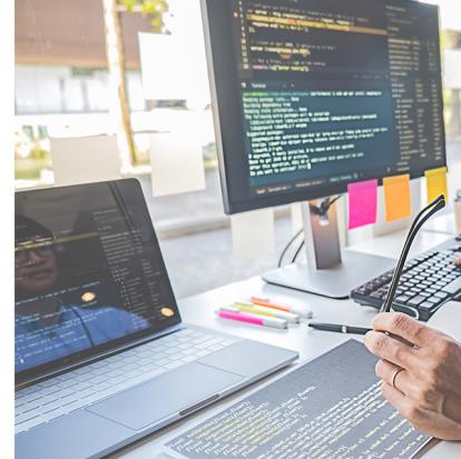 a person looking over code on a laptop, monitor and tablet at a desk