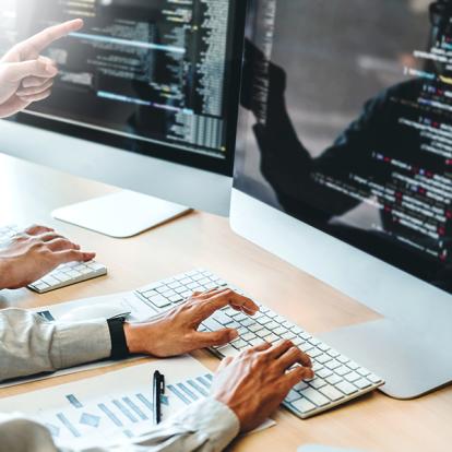 two people working on code on monitors beside each other
