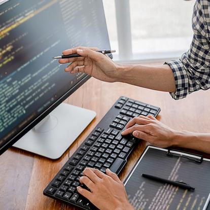 two people working on code on a desktop screen and a tablet