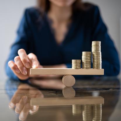 a person balancing a wooden scale with her hand while coins sit on the other side