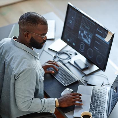 a man working on a dual monitor setup looking at charts