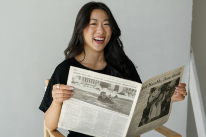 Marisa Chen sits in a chair, smiling and reading a newspaper