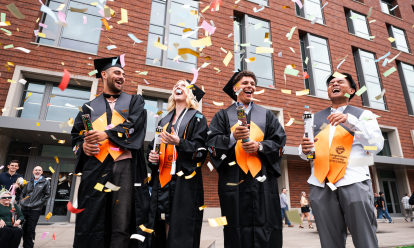 Four students wearing graduation regalia celebrate at Austin Hall among paper streamers