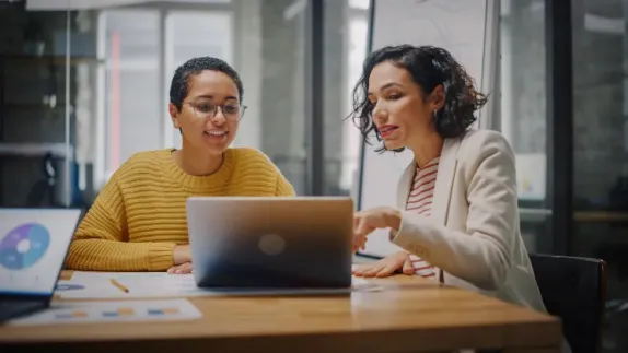 Two women sitting at a laptop discussing finances