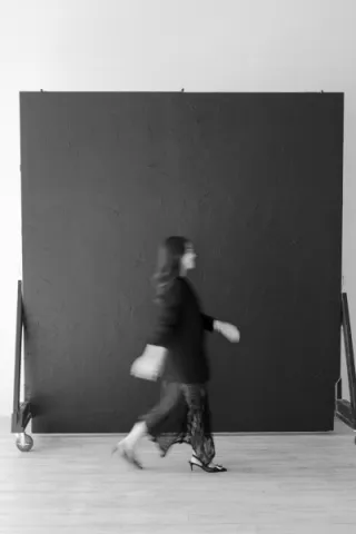 Blurred picture of Marisa Chen walking in front of a black screen wearing a black blazer and lace skirt. 