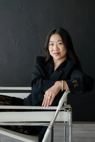 Marisa Chen wears a black blazer and lace top in front of a black background