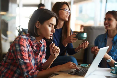 woman studying on laptop with two other women drinking coffee